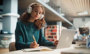 Junge Frau mit Kopfhörern und Laptop in der Bibliothek