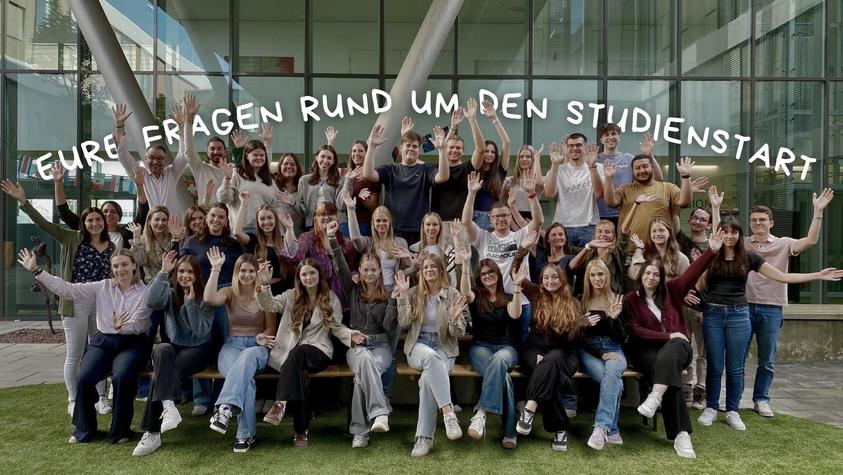 Studienanfänger mit erhobenen Händen vor einem Gebäude